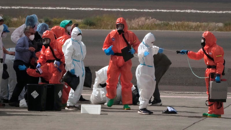 Passengers are sprayed with disinfectant by Spanish government officials before boarding a...